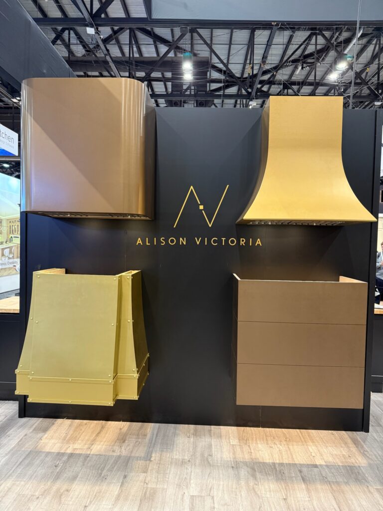 The image shows four different range hoods in varying shapes. One is a box-style hood featuring horizontal shiplap. Another one is  A box style hood with curved edges and wrapped in chocolate. brass color. The other range hood is fluted in liquid copper finish, and the last range hood is Paulina range hood in liquid copper finish. 
