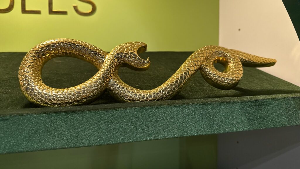 Brass snake figurine  posed in a coiled, winding position. Its head is raised with its mouth open, revealing small fangs, giving an aggressive or striking pose. 