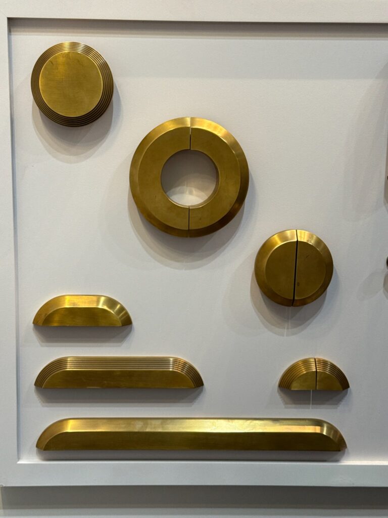 Luxury brass cabinet pulls with curves. Three different cup pull handles are shown in varying lengths. Each one has a smooth surface and curved edges. There are also three circular pulls. Refined tiered stepped details envelop the edges of each piece. There is also 