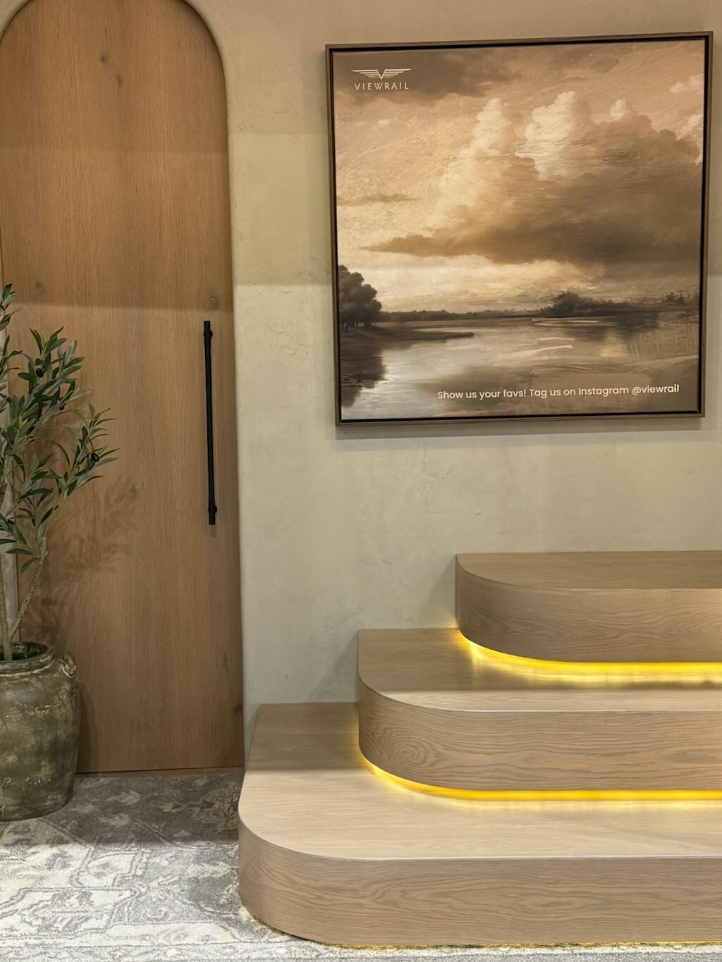 Modern interior staircase lighting using LED strips installed under the tread nosing. Arched door in light oak with bronze vertical handle. Cloud artwork in black picture frame.