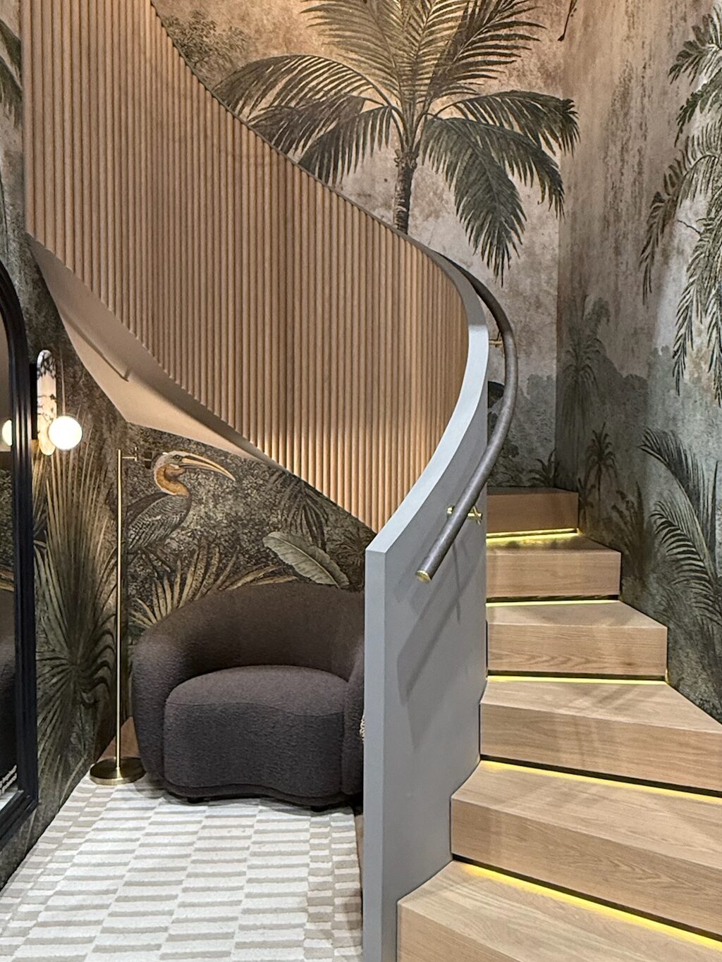 Curved staircase with LED lighting under the tread nosing. Tropical wallpaper covers the walls.  There is a black railing. 