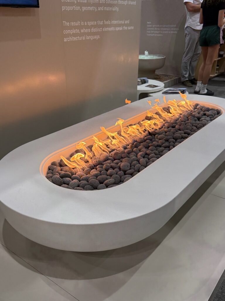 Arched concrete outdoor gas fireplace with flames running down the middle of it. There are dark gray rocks inside. 